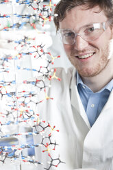 Germany, Portrait of young scientist with DNA model, smiling - FLF000274