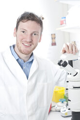 Deutschland, Porträt eines jungen Wissenschaftlers mit Mikroskop im Labor, lächelnd - FLF000285