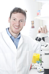 Germany, Portrait of young scientist with microscope in laboratory, smiling - FLF000285