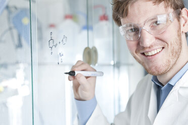 Deutschland, Porträt eines jungen Wissenschaftlers, der eine chemische Gleichung auf ein Glas schreibt, lächelnd - FLF000289
