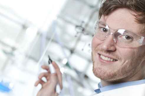 Deutschland, Porträt eines jungen Wissenschaftlers, der sich Notizen macht, lächelnd - FLF000290