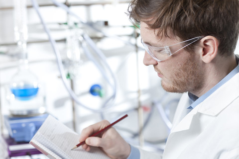 Deutschland, Porträt eines jungen Wissenschaftlers, der lächelnd Notizen in einem Heft macht, lizenzfreies Stockfoto