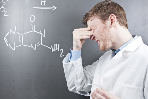 Deutschland, Junge Wissenschaftlerin mit ernstem Gesichtsausdruck und chemischer Gleichung auf Kreidetafel, lizenzfreies Stockfoto