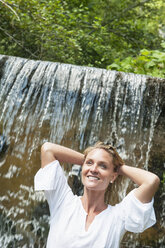 Österreich, Altenmarkt-Zauchensee, Mittlere erwachsene Frau entspannt sich am Wasserfall, lächelnd - HHF004459