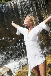 Österreich, Altenmarkt-Zauchensee, Mittlere erwachsene Frau entspannt sich am Wasserfall, lächelnd - HHF004460