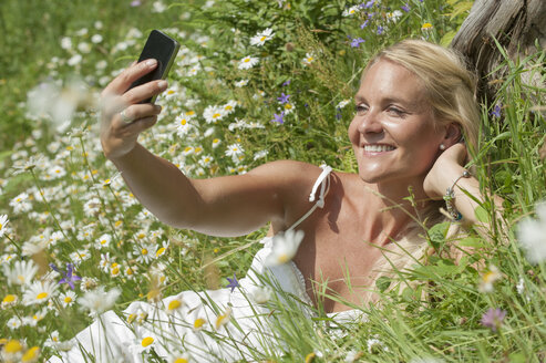 Österreich, Salzburg, Mittlere erwachsene Frau mit Mobiltelefon auf einer Wiese, lächelnd - HHF004471