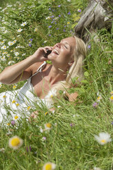 Österreich, Salzburg, Mittlere erwachsene Frau, die auf einer Wiese mit einem Handy telefoniert, lächelnd - HHF004472