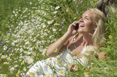 Österreich, Salzburg, Mittlere erwachsene Frau, die auf einer Wiese mit einem Handy telefoniert, lächelnd - HHF004473