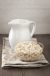 Milk jar with bowl of oat flakes on wooden table, close up - EVGF000061