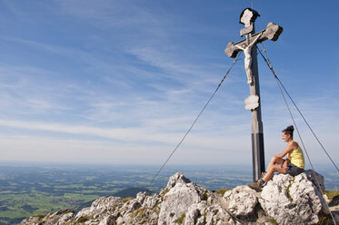 Deutschland, Bayern, Mittlere erwachsene Frau sitzend auf Berggipfel mit Kreuz - UMF000591