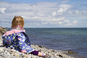 Dänemark, Mädchen sitzt am Strand und blickt über blaues Wasser - JFEF000028