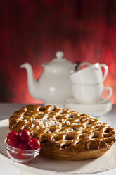 Gittertorte mit Kirschen und Zuckerkristallen und Teekanne im Hintergrund - CSF017362