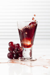 Glass with splashing red grape juice, close up - CSF017426