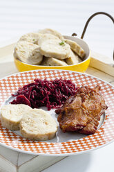 Plate of pork knucke with slices of bread dumpling and red cabbage in wooden tray, close up - CSF017596