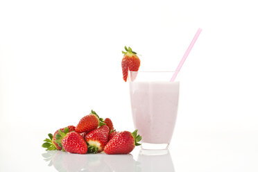 Glass of strawberry milk shake besides strawberries on white background, close up - MAEF006074