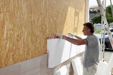 Europe, Germany, Rhineland Palatinate, Man sticking polystyrene on wooden house wall - CSF017668