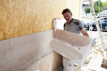 Europe, Germany, Rhineland Palatinate, Man sticking polystyrene on wooden house wall - CSF017669