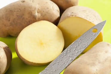 Raw potatoes with knife on chopping board, close up - CSF017659