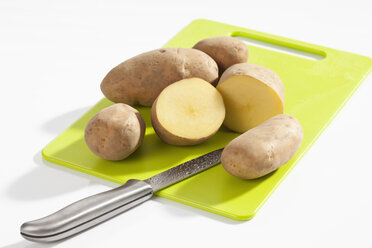 Raw potatoes with knife on chopping board, close up - CSF017610