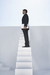 Geschäftsmann im schwarzen Anzug mit Laptop auf einer Treppe stehend - PDYF000381