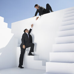 Businessman helping another man to climb stairs - PDYF000403