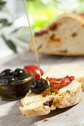 Gießen von Olivenöl auf eine Scheibe Brot mit Oliven und getrockneten Tomaten, Nahaufnahme - CSF017747