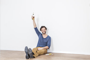 Porträt eines Mannes, der mit einer Bierflasche auf dem Boden sitzt und lächelt - FMKF000567