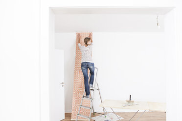 Woman sticking wallpaper on wall - FMKF000631