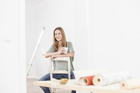 Woman sitting on chair with cup, wallpaper on table in foreground stock photo