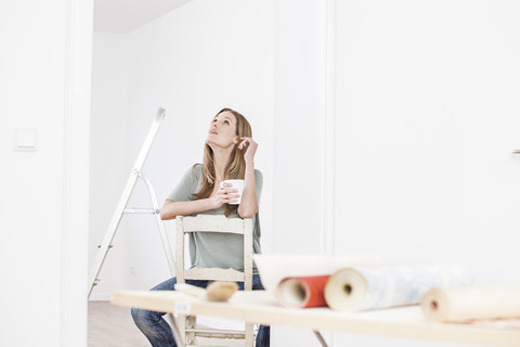 Frau auf Stuhl sitzend mit Tasse, Tapete auf Tisch im Vordergrund, lizenzfreies Stockfoto