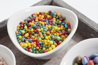 Variety of sprinkles in bowl on wooden tray, close up - CSF017924