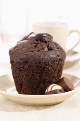 Teller mit Schokoladenmuffin mit Praline, Kaffeetasse im Hintergrund - CSF017944