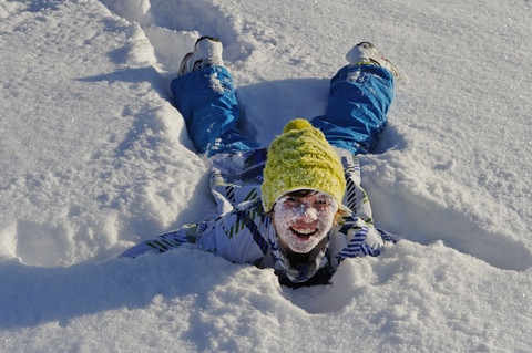 Deutschland, Bayern, Junge liegend im Schnee, lächelnd, lizenzfreies Stockfoto