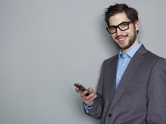 Porträt eines lächelnden Geschäftsmannes, der ein Mobiltelefon hält - STKF000232