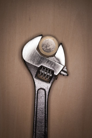 Adjustable spanner with euro coin on wooden background stock photo