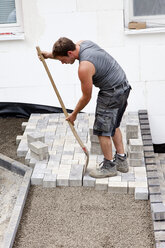 Germany, Rhineland Palatinate, Young man adjusting paving stone - CSF018064