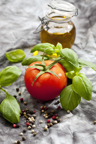 Strauchtomate mit Basilikumkraut, bunten Pfefferkörnern und Glas mit Olivenöl auf grauem Hintergrund, Nahaufnahme, lizenzfreies Stockfoto