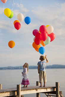 Deutschland, Bayern, Junge und Mädchen stehen auf dem Steg und lassen Luftballons am Starnberger See steigen - HSIF000285