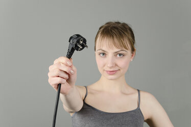 Porträt einer jungen Frau mit Netzstecker vor grauem Hintergrund - ONF000060