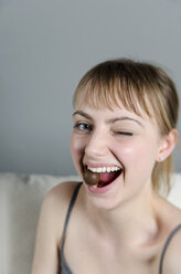 Portrait of young woman eating chocolate praline, smiling - ONF000069