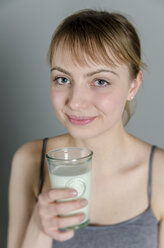Portrait of young woman holding glass of milk, smiling - ONF000070