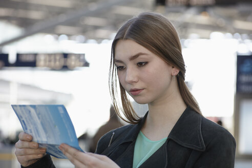 Deutschland, Köln, Teenager-Mädchen schaut auf Ticket im Flughafen - RHYF000344