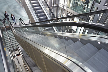 Germany, Cologne, Young woman and mature man moving up escalator at airport - RHYF000349