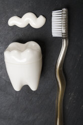 Zahnförmiger Kunststoffbehälter, Zahnbürste und Zahnpasta auf Schiefertafel, Nahaufnahme - TDF000039