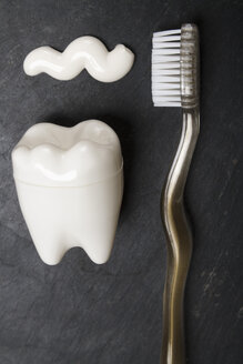 Tooth shaped plastic container, tooth brush and tooth paste on slate board, close up - TDF000039