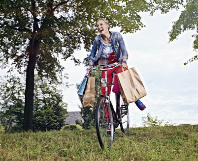 Deutschland, Köln, Junge Frau auf Fahrrad mit Einkaufstüten - RHYF000353