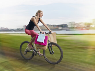 Deutschland, Köln, Junge Frau auf Fahrrad mit Einkaufstüten - RHYF000374