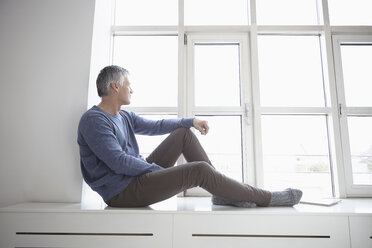 Germany, Bavaria, Munich, Mature man sitting at window, looking away - RBF001313