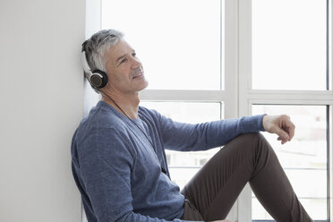 Deutschland, Bayern, München, Älterer Mann sitzt am Fenster mit Musik, lächelnd - RBF001307