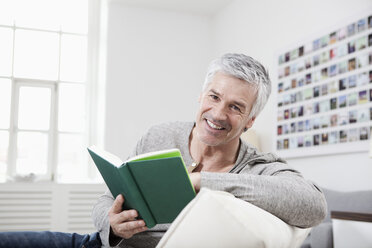 Germany, Bavaria, Munich, Portrait of mature man reading book on couch, smiling - RBF001253
